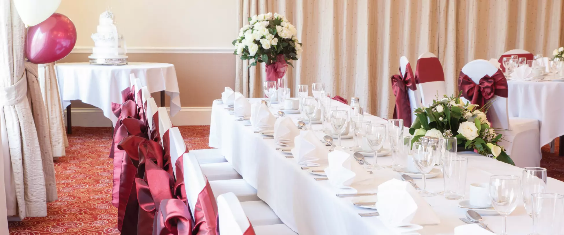 A wedding table set up for the bridal party with white table cloths, red ribbons, and bouquets of white flowers.